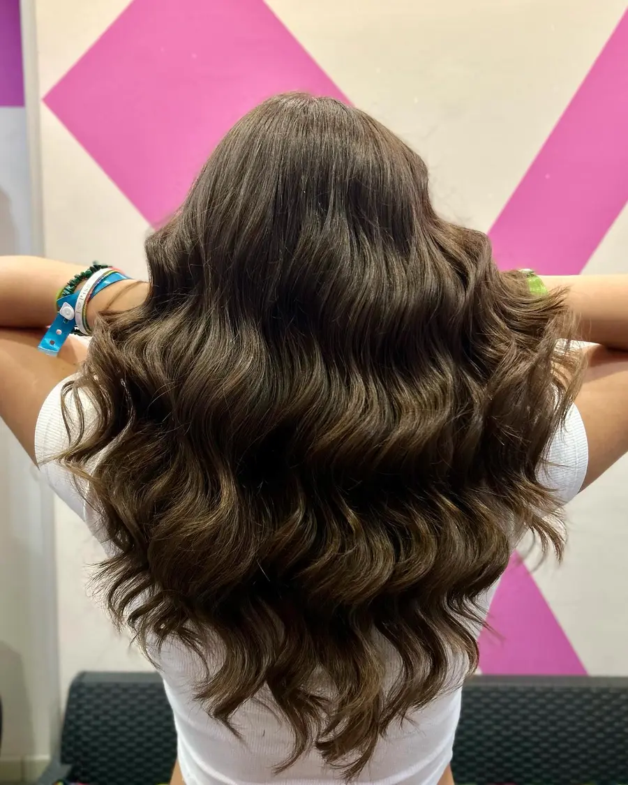 Piega a onde su capelli castani, davanti alla parete rosa del salone